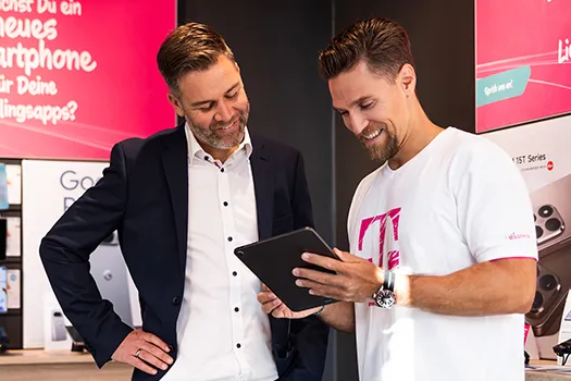 Beratung im Telekom Shop: zwei Männer sehen Tablet-Angebot für Smartphone an