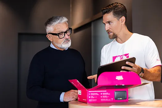 Mitarbeiter erklärt Kunde am Tresen ein neues Smartphone im Telekom Shop